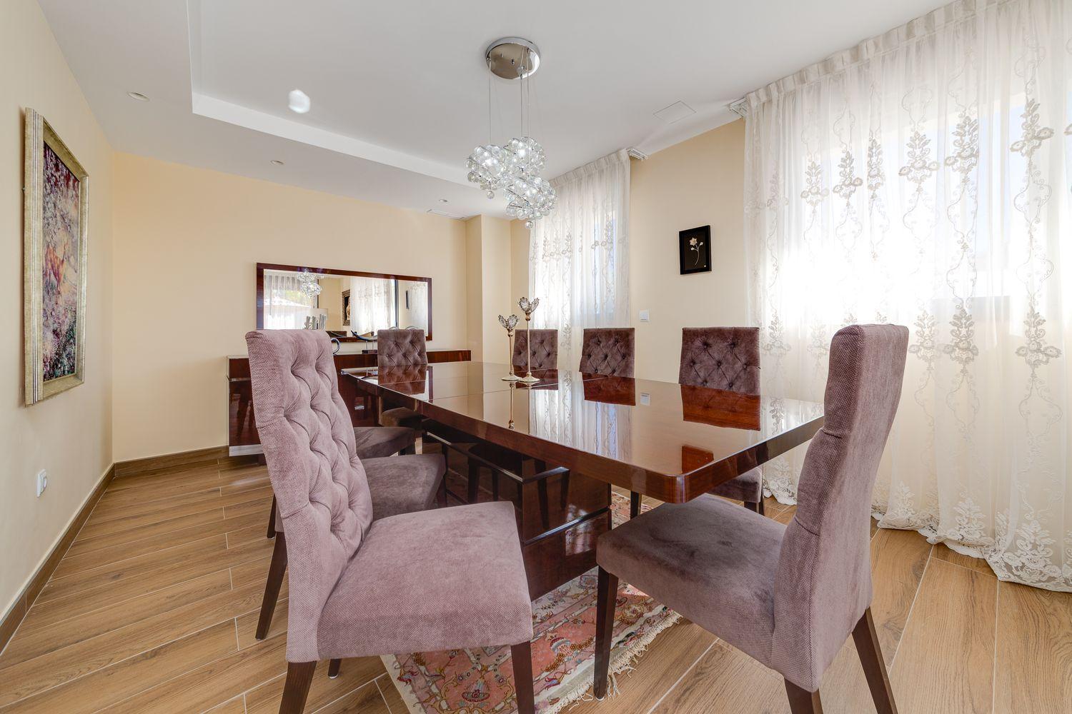 Elegant dining room with a glossy wooden table, tufted lavender chairs, and a crystal chandelier.