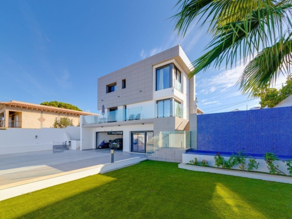 Modern white multi‑story house with glass balconies, a blue tiled wall, and a green lawn under a clear sky.