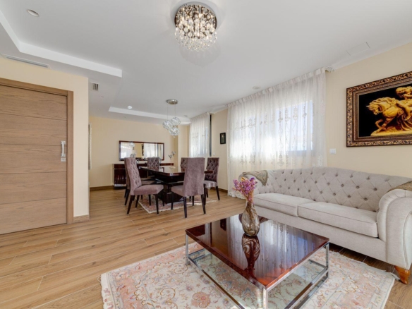 Open living and dining room with a beige tufted sofa, dark wood dining table, and a glass coffee table on a warm wood floor