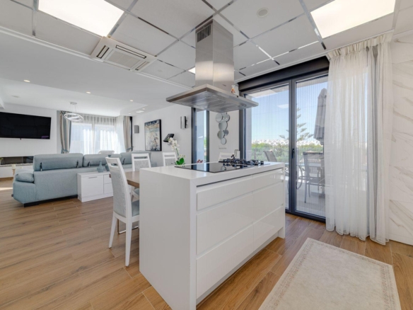 Open-concept kitchen and living area with a white island, stainless range hood, and a sliding glass door to a balcony.
