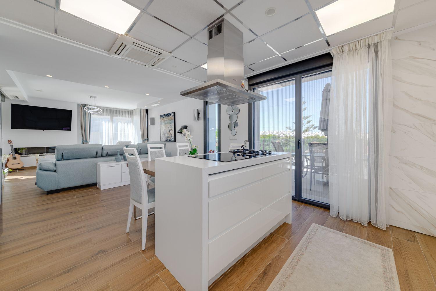 Open-concept kitchen and living area with a white island, stainless range hood, and a sliding glass door to a balcony.