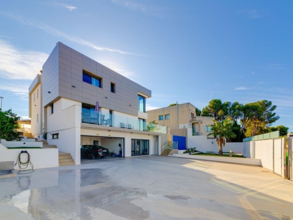 Modern white three-story house with glass balcony and driveway, blue sky in the background
