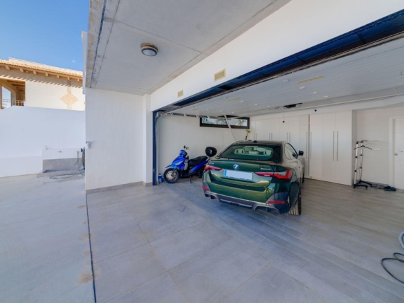 Open garage with a green BMW sedan and a blue scooter parked inside, white storage cabinets along the back wall.