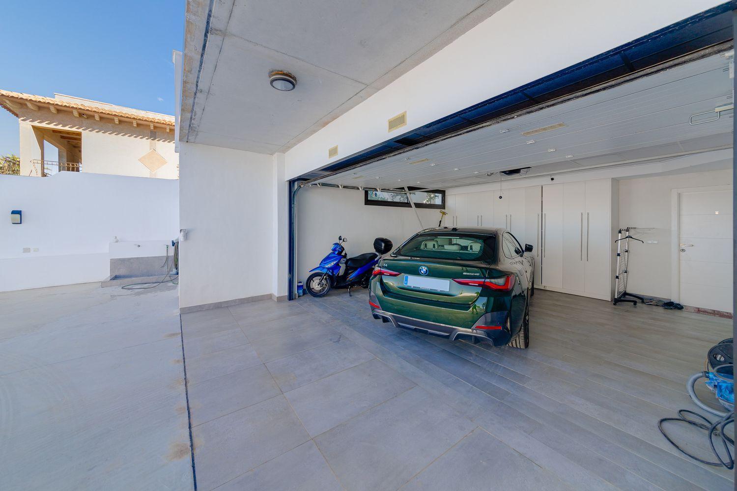 Open garage with a green BMW sedan and a blue scooter parked inside, white storage cabinets along the back wall.
