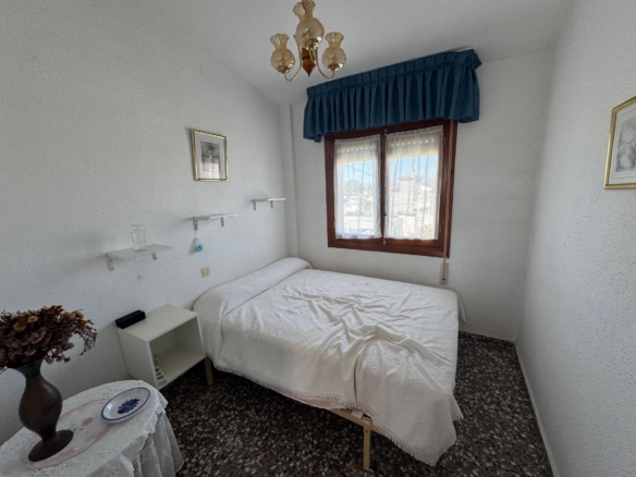 Small bedroom with two single beds, white quilts, a blue window valance, and a chandelier above.