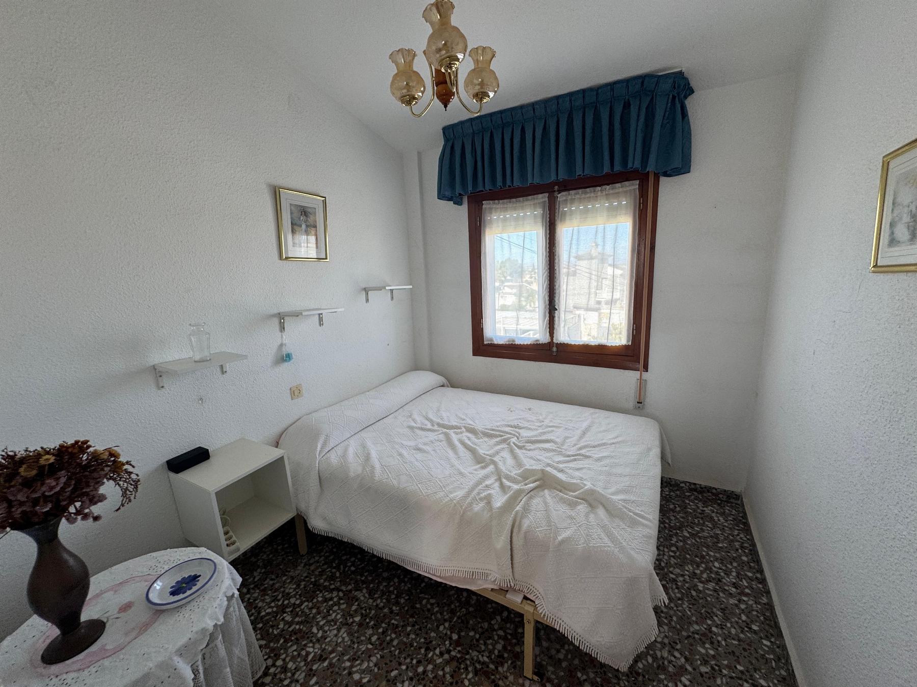 Small bedroom with two single beds, white quilts, a blue window valance, and a chandelier above.