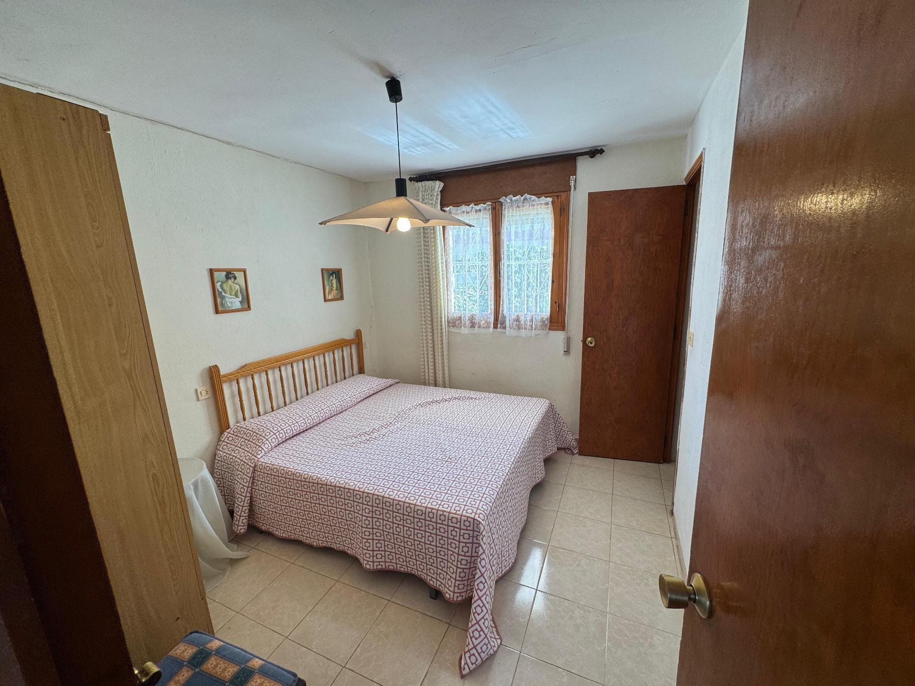 Twin-bed bedroom with patterned bedspreads, wooden headboard, and a hanging ceiling light; window with lace curtains on the far wall