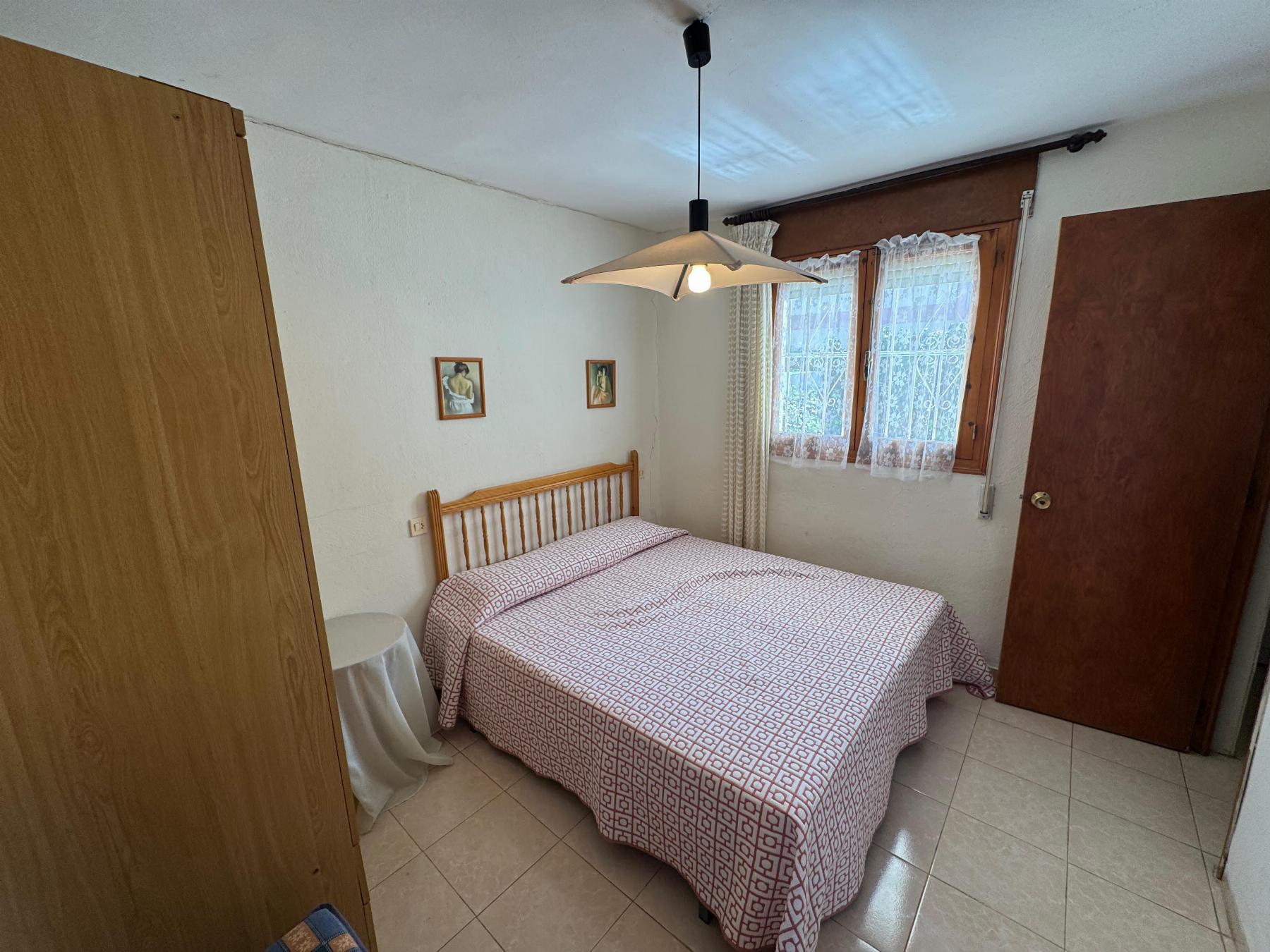 Twin bedroom with two single beds pushed together, wooden headboard, matching geometric bedspreads, wardrobe, and a window with lace curtains.