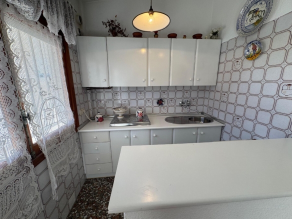 Small vintage kitchen with white cabinets, lace curtains, and a stainless sink.