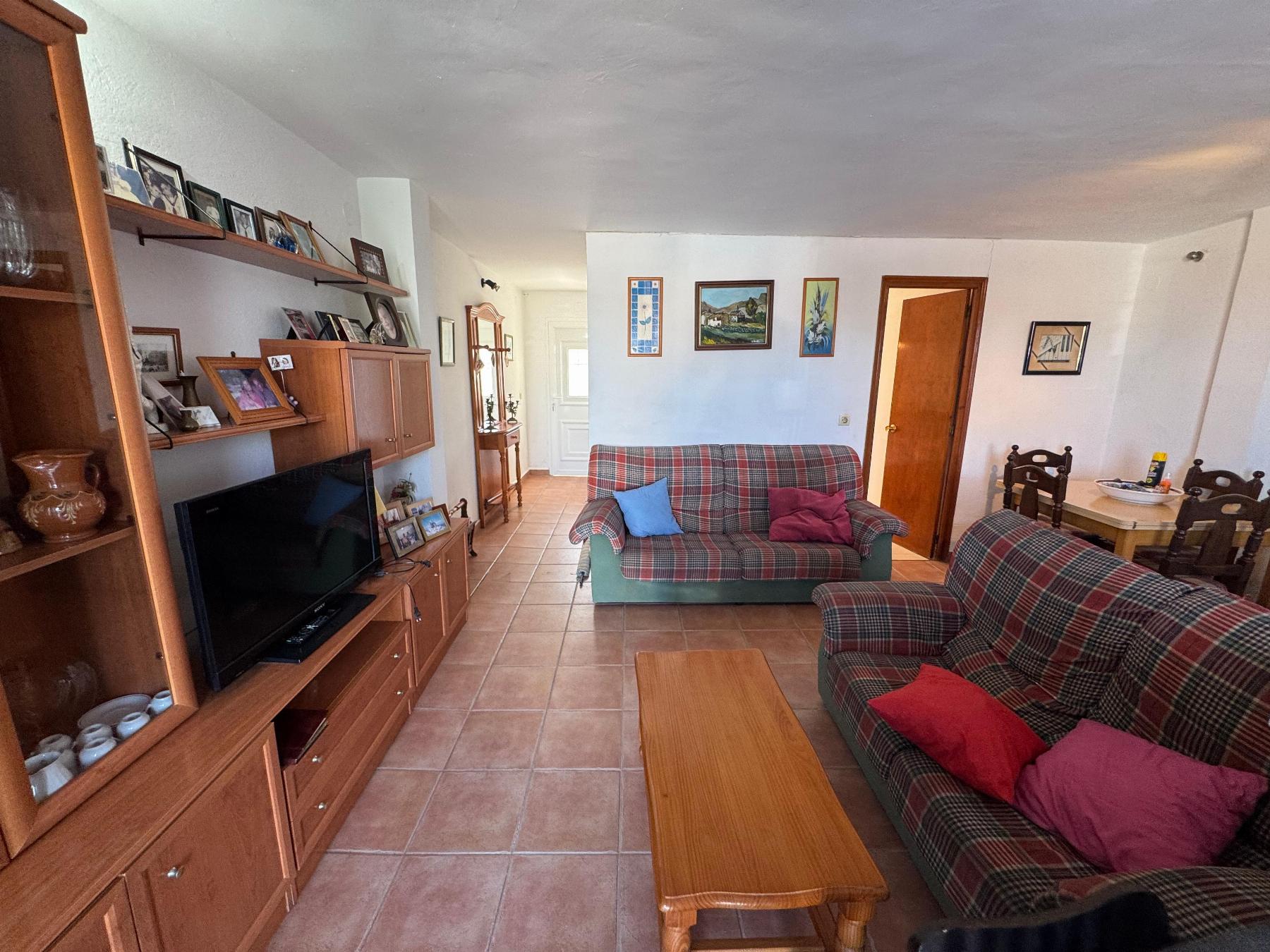 Cozy living room with plaid green and red sofa, wooden coffee table, and built‑in shelves filled with photos and knickknacks.