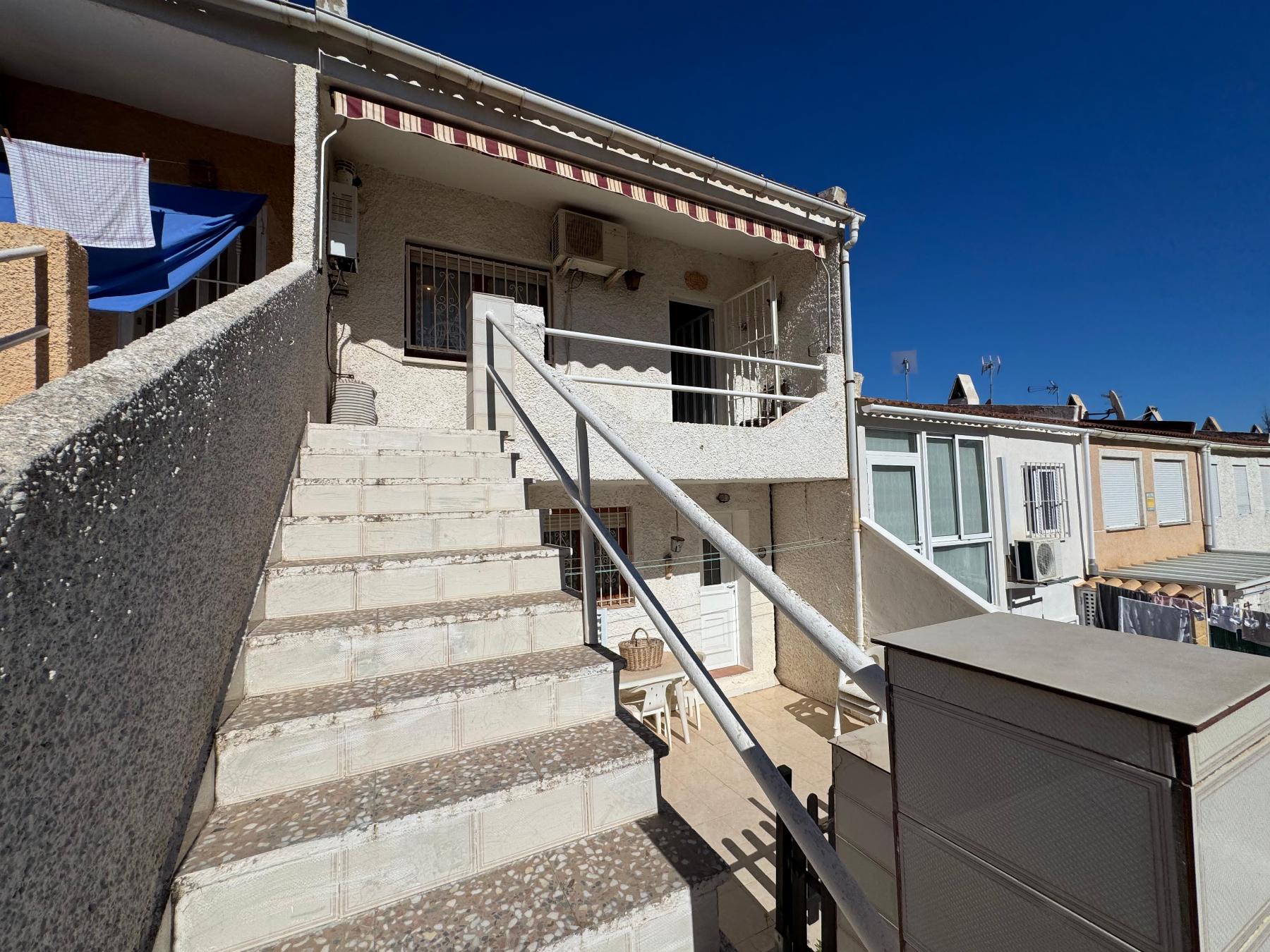 Exterior stairway leading to an upper-floor apartment, with white textured walls, a metal handrail, and laundry hanging on the left against a clear blue sky