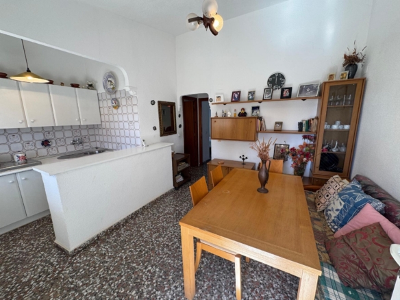 Open-plan kitchen and dining area with white cabinets, tiled backsplash, a sink, and a wooden dining table with a sofa nearby.