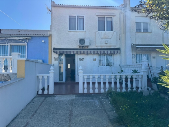 White two-story house with a blue side wall, barred windows, and butterfly decorations near the entrance; tiled walkway and white rail fence in front.