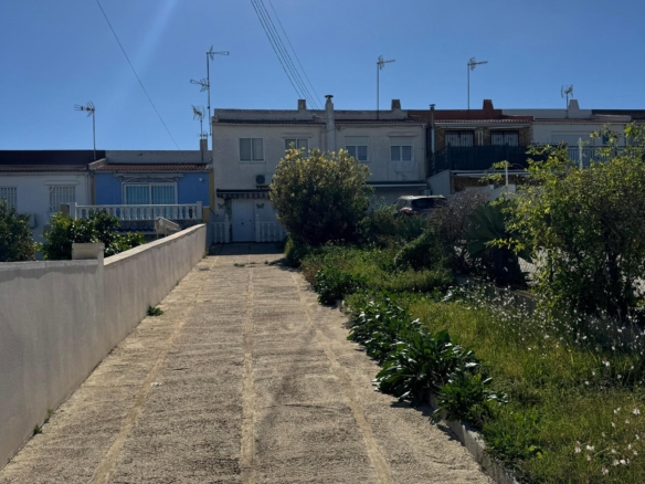 Long concrete driveway slopes upward toward a row of white houses under a bright blue sky with a sun flare and overhead power lines.
