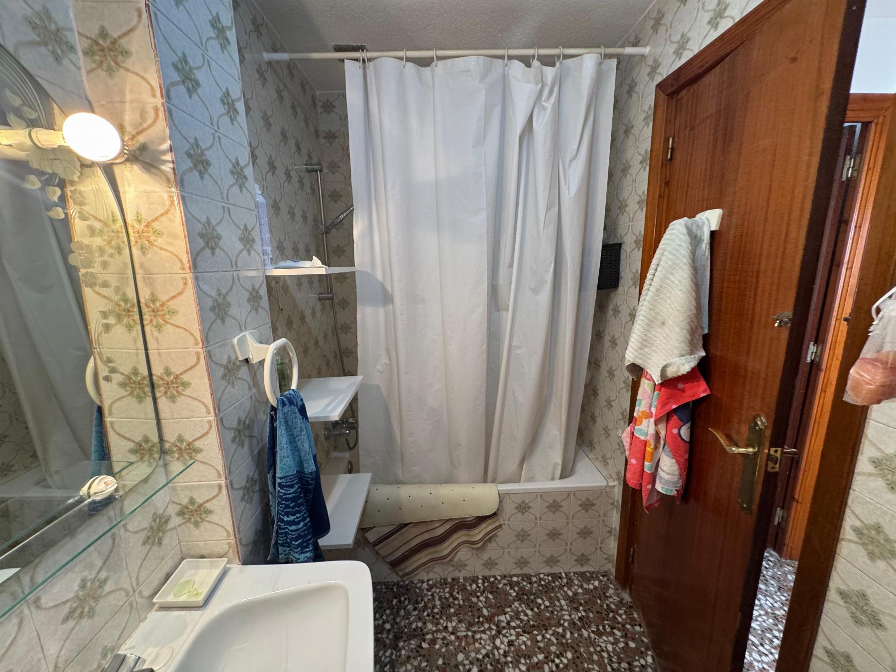 Small vintage bathroom with patterned tiles, white shower curtain, and towels by a wooden door.