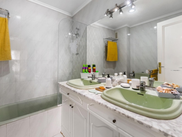 Double-sink bathroom vanity with a marble countertop and green sinks, yellow towels, and a large mirror.