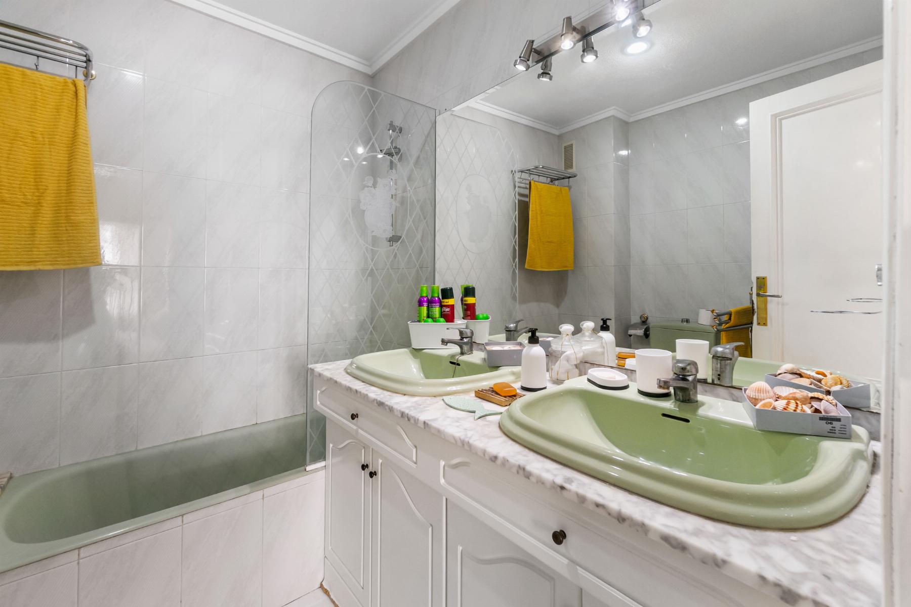 Double-sink bathroom vanity with a marble countertop and green sinks, yellow towels, and a large mirror.