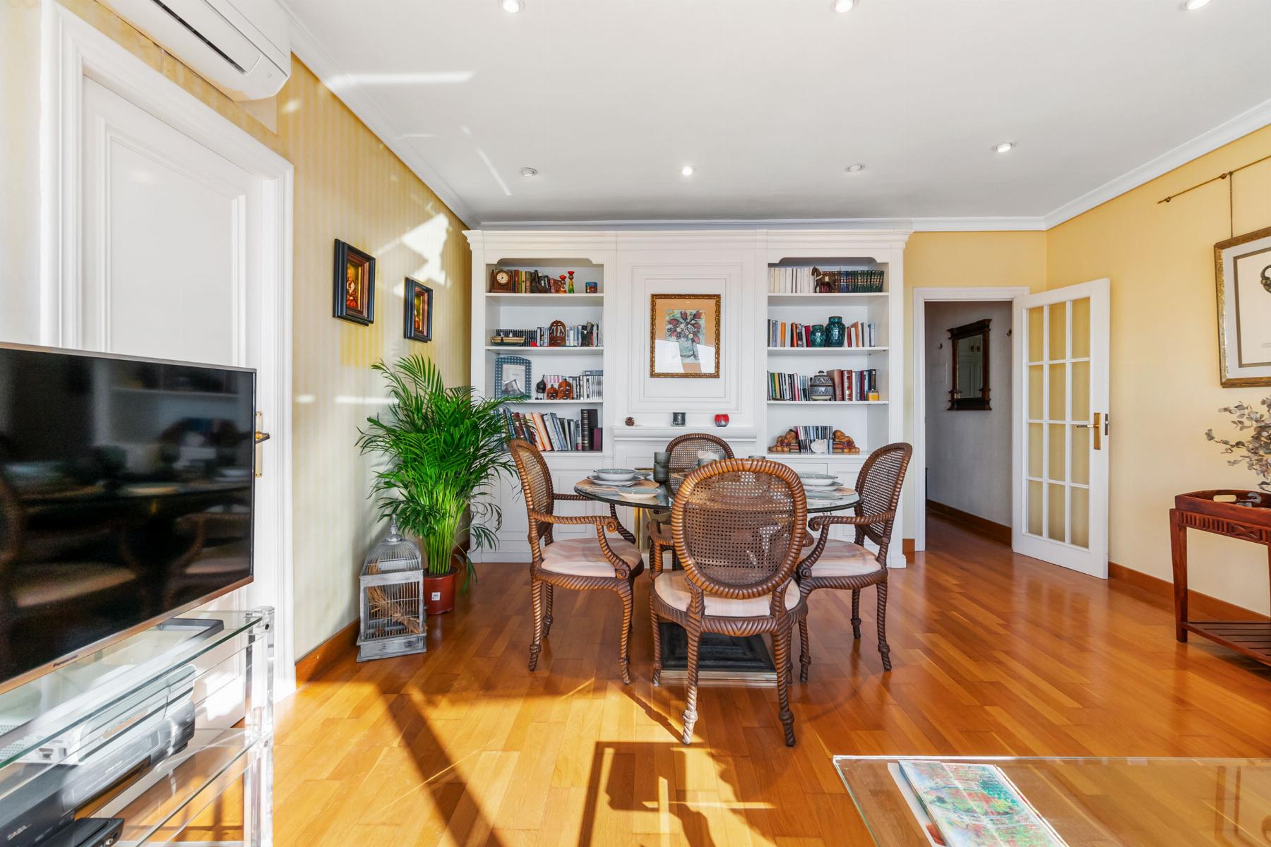 Bright living-dining room with white built-in cabinets, round glass table, wicker chairs, and warm yellow walls. Linear hardwood floor.