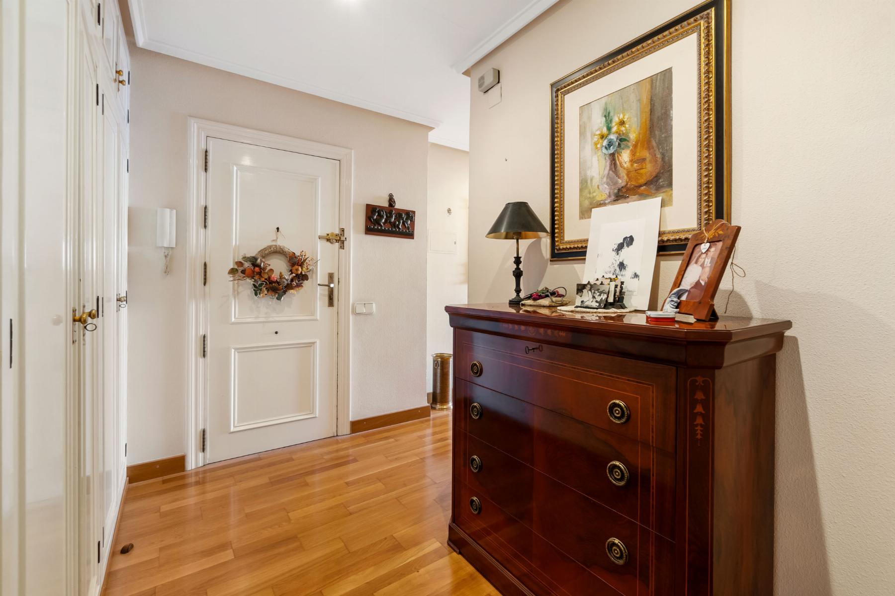 Hallway with white doors on left, a wreath on the front door, and a polished wooden dresser against the right wall topped with a lamp and framed art.