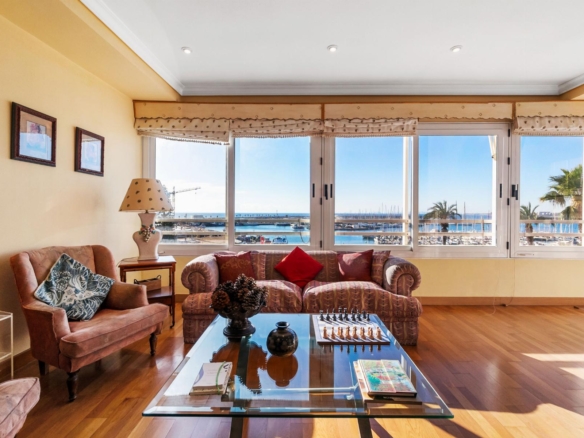 Living room with pink upholstered sofas facing large windows overlooking a marina and ocean view; glass coffee table and decorative items nearby