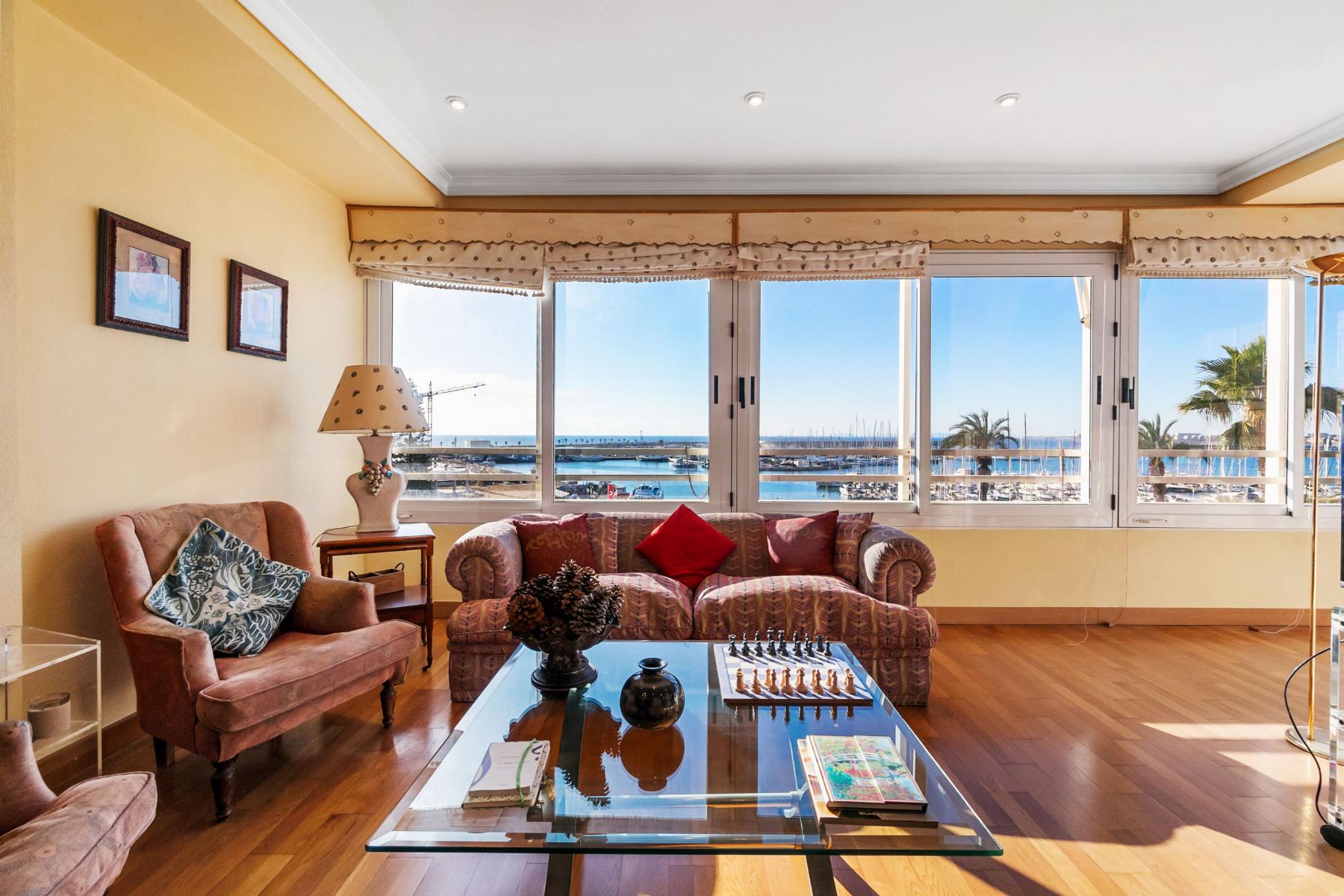 Living room with pink upholstered sofas facing large windows overlooking a marina and ocean view; glass coffee table and decorative items nearby