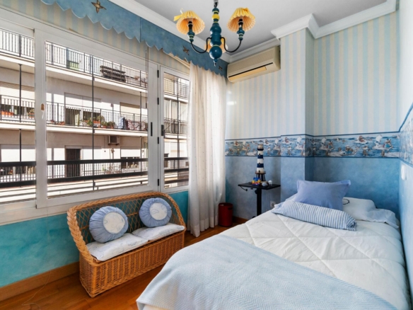 Bright nautical‑themed bedroom with blue stripes, twin beds, a wicker bench, and large windows opening to a balcony.