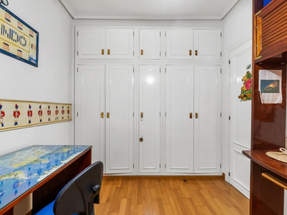 Study nook with tall white storage cabinets, a world map desk, and wooden floor; colorful wall art on left and shelves on right.