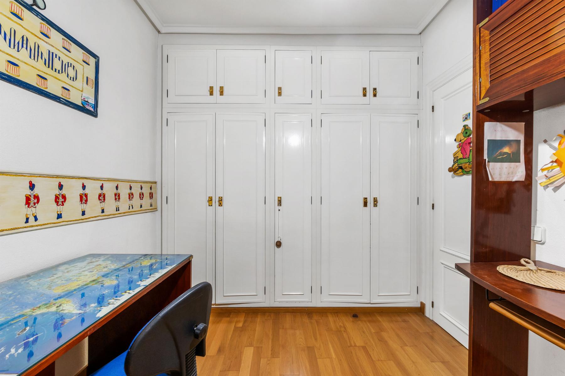 Study nook with tall white storage cabinets, a world map desk, and wooden floor; colorful wall art on left and shelves on right.