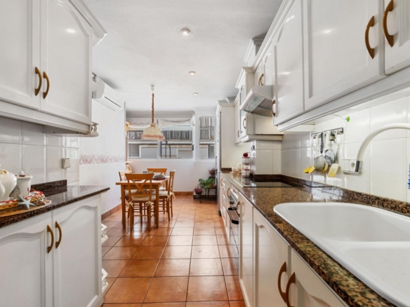 Bright white kitchen with brown granite countertops and a dining table seen at the far end.