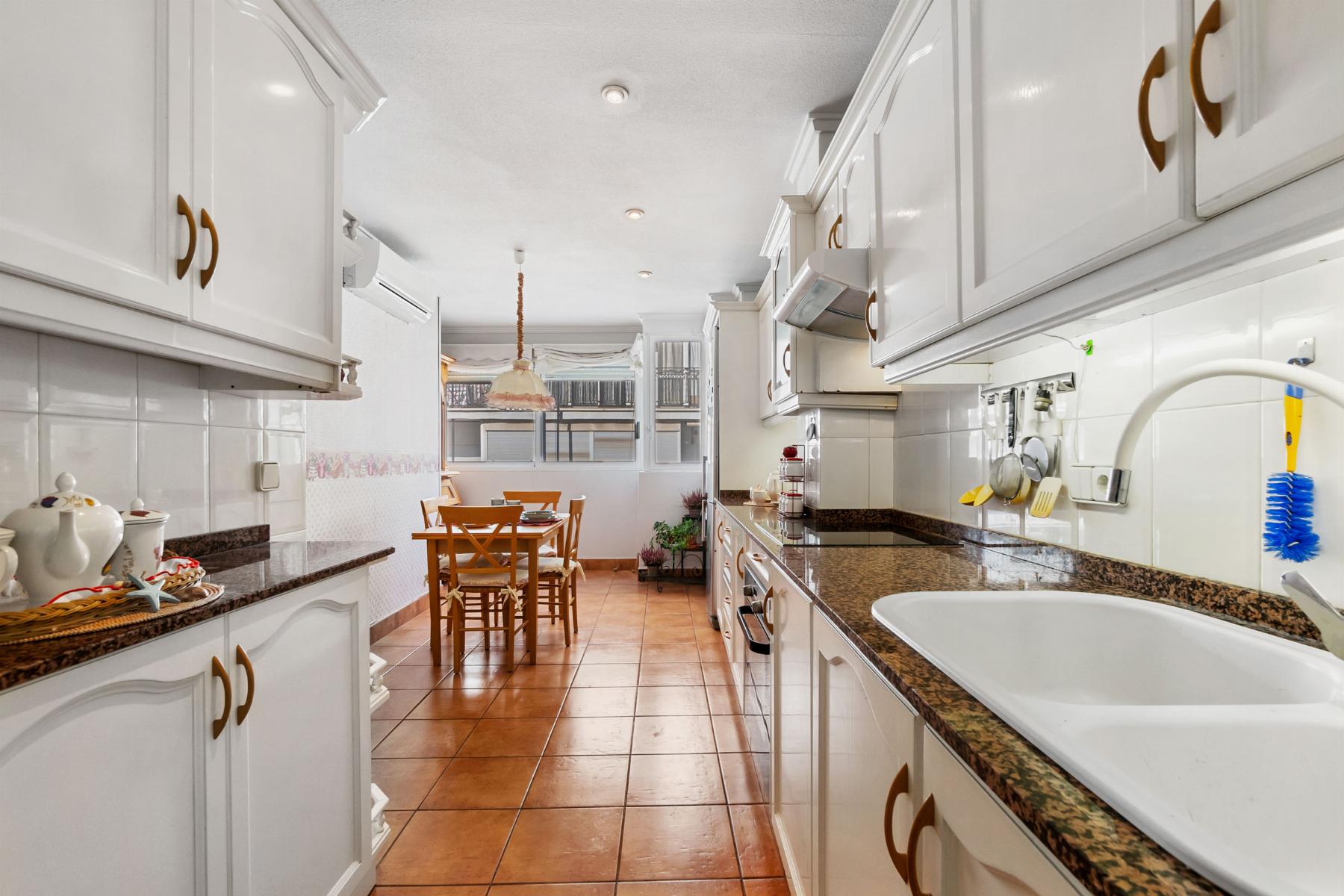 Bright white kitchen with brown granite countertops and a dining table seen at the far end.