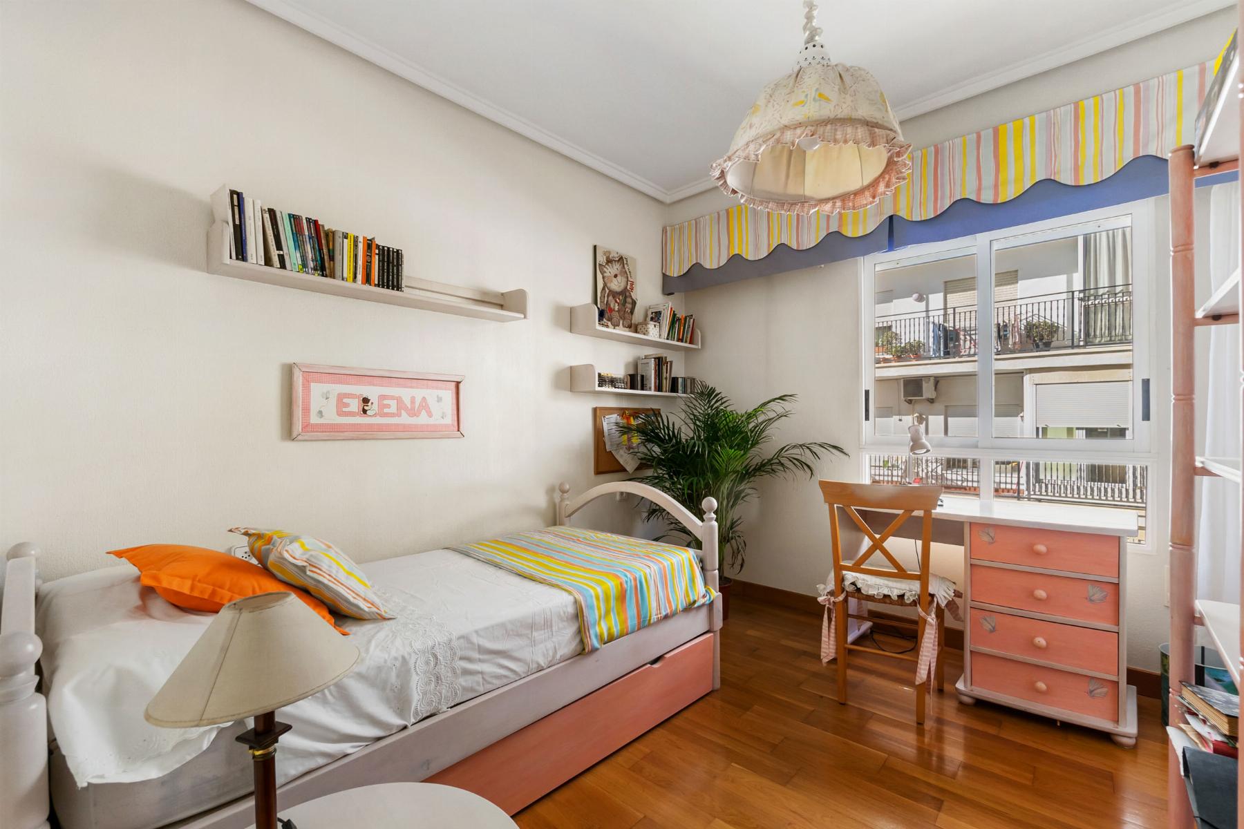 Bright girl's bedroom with white walls, striped rainbow bedding, and a window view of a balcony corner. (informative)