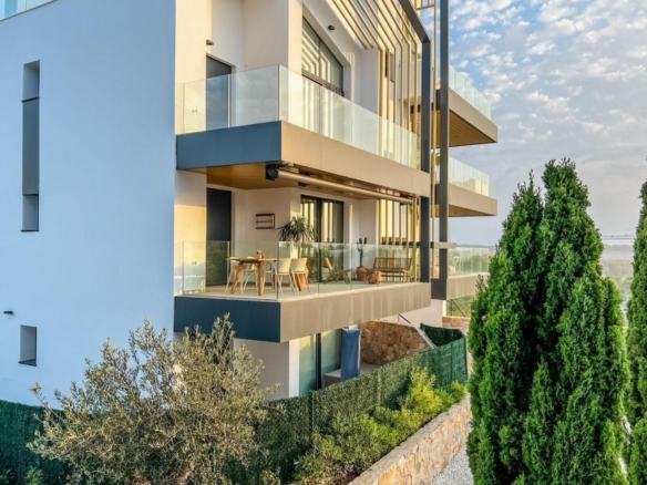 Modern apartment building with glass balconies and an outdoor dining area on a sunlit terrace.