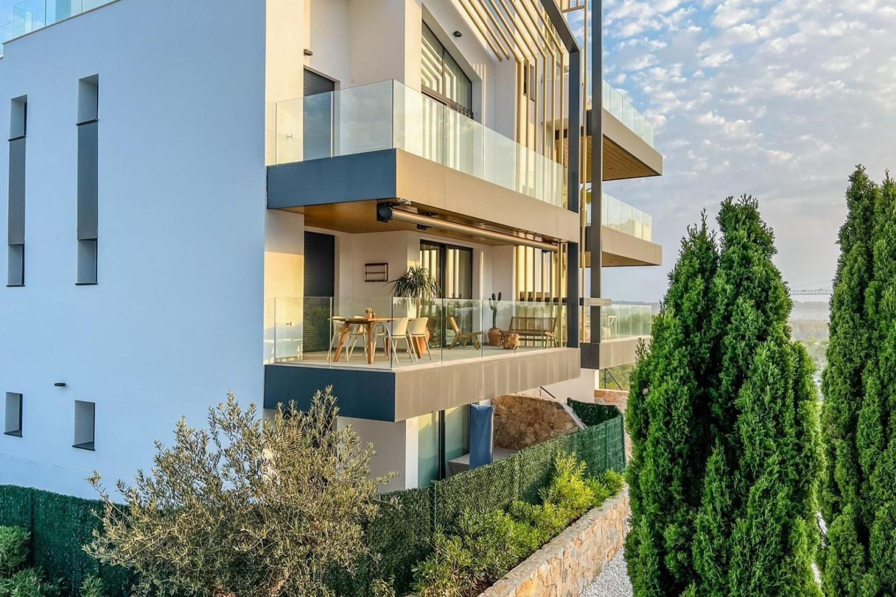 Modern apartment building with glass balconies and an outdoor dining area on a sunlit terrace.