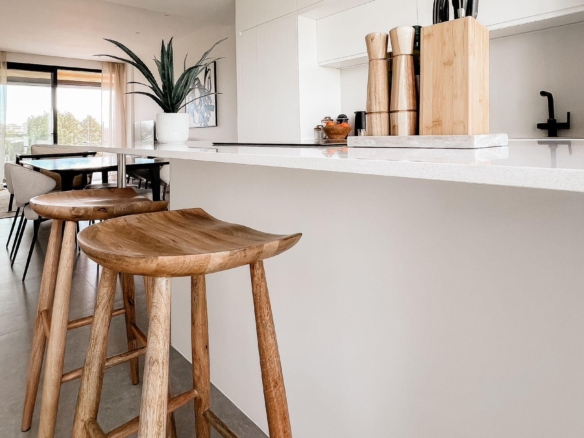 Modern white kitchen with marble countertop, wooden bar stools, and a knife block on the island.