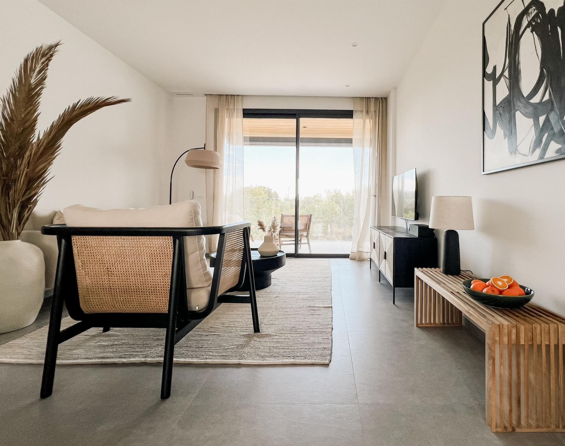 Bright modern living room with woven chairs facing a sliding glass door to a balcony and a rug-lined floor.