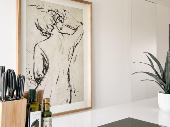 Kitchen counter with a wooden knife block, two bottles of olive oil, and a framed abstract line-art poster leaning against a white wall.
