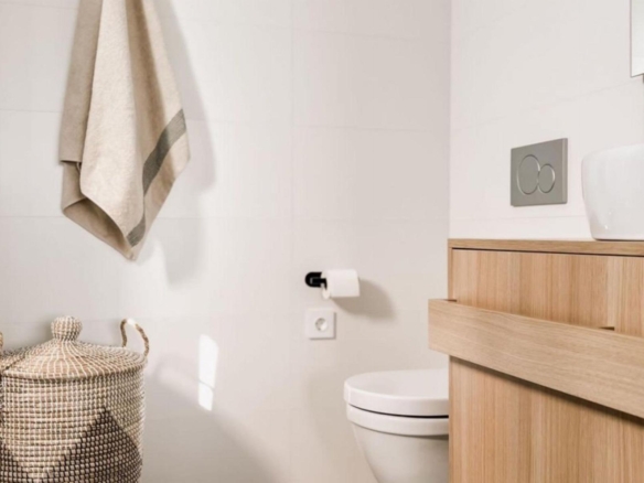 Modern bathroom scene with a hanging beige towel, wicker basket, and a light wood vanity beside a wall-mounted toilet.