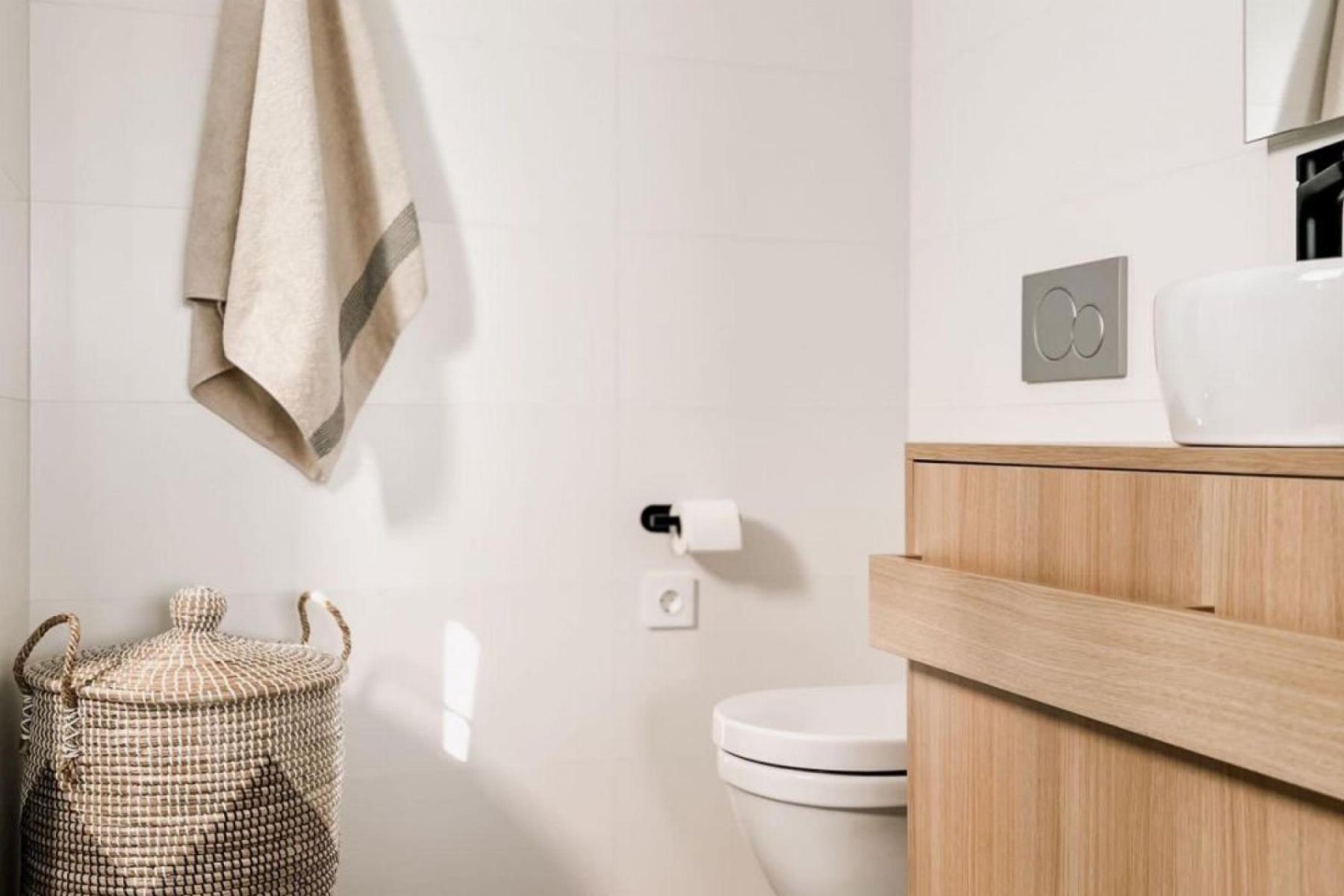 Modern bathroom scene with a hanging beige towel, wicker basket, and a light wood vanity beside a wall-mounted toilet.