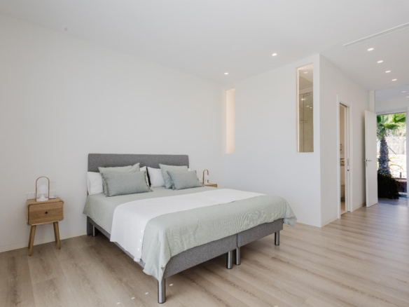 Minimalist bedroom with a gray upholstered bed, pale green bedding, light wood floor, and open doorway to outdoors.
