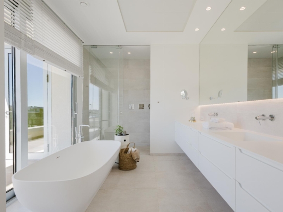 Bright minimalist bathroom with a freestanding oval tub, glass shower, and long white vanity beneath bright windows.