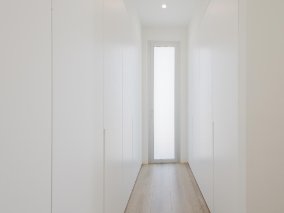 Bright, minimalist white hallway lined with tall wardrobes on both sides, ending with a frosted glass door at the far end.
