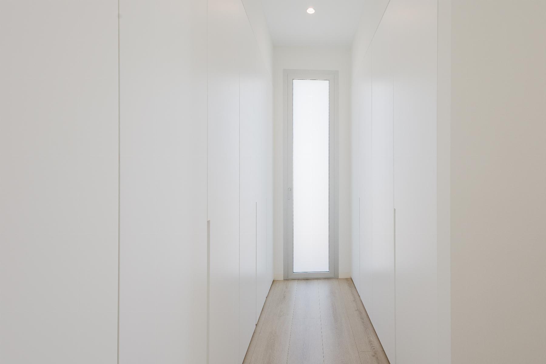 Bright, minimalist white hallway lined with tall wardrobes on both sides, ending with a frosted glass door at the far end.