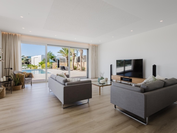 Bright contemporary living room with gray sofas, a large TV, and sliding glass doors opening to a sunny backyard and pool area.
