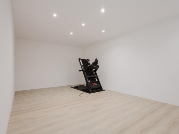 Minimal home gym: white-walled room with light wood floor and a black treadmill on a mat against the back wall.