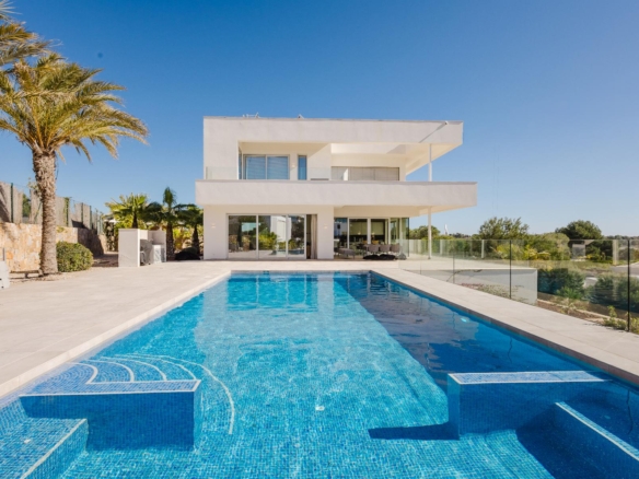 Contemporary white two‑story house with a large rectangular pool in the foreground and palm trees under a clear blue sky.