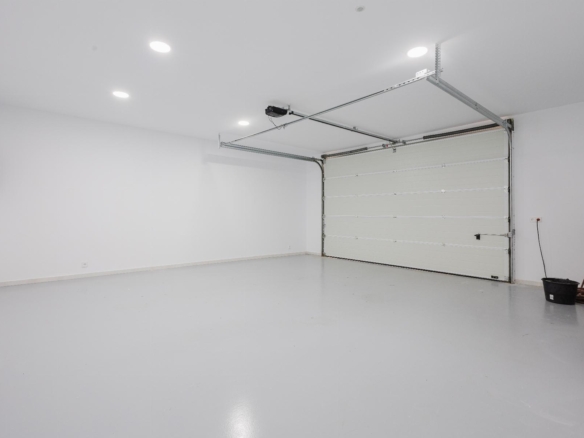 Empty home garage with a white interior, closed sectional door, and bright recessed ceiling lights.
