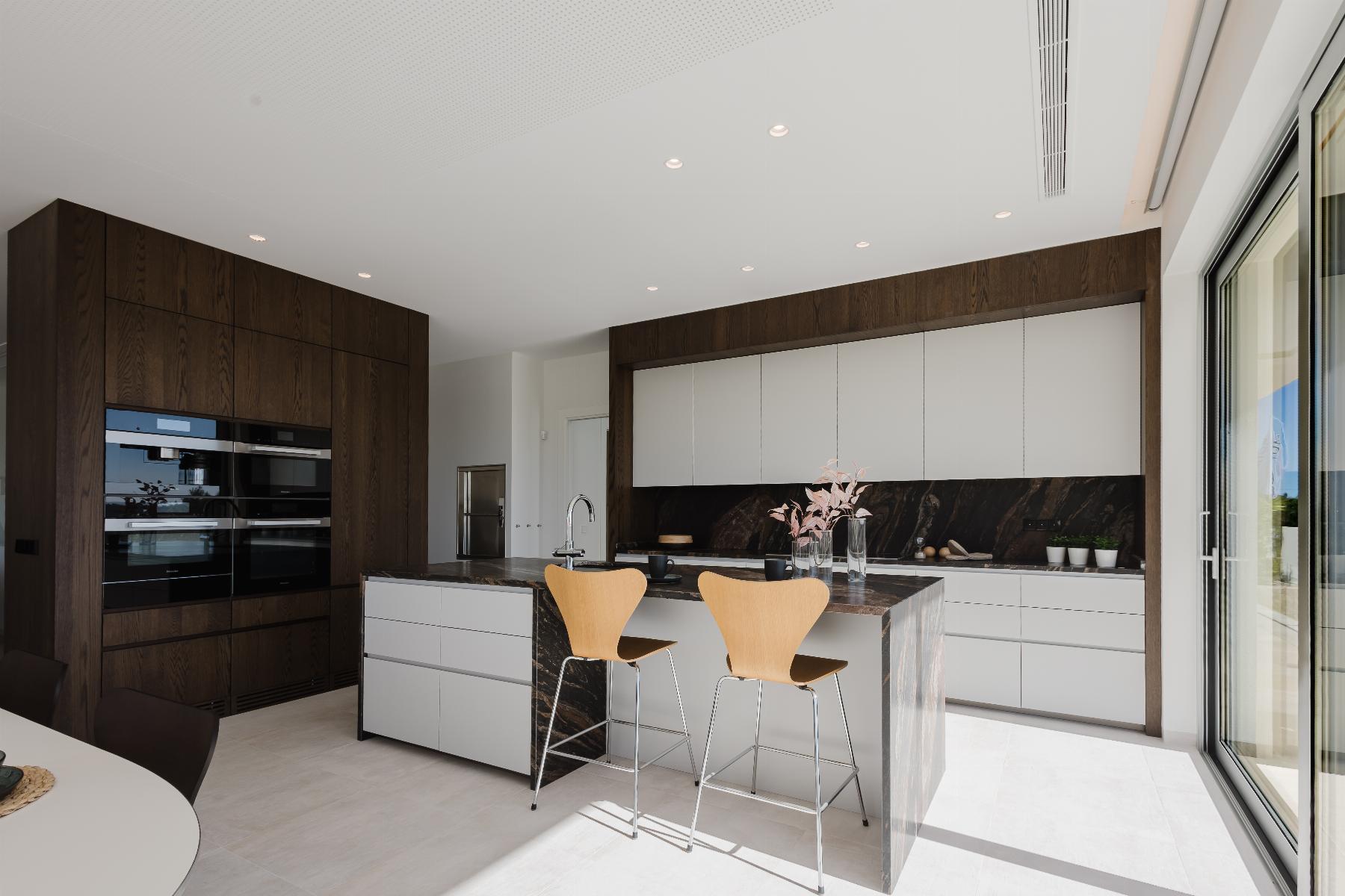 Modern kitchen with dark wood cabinetry, white upper cabinets, and a marble island with two wooden bar stools.
