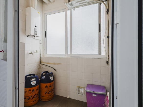 Utility room with two orange gas cylinders on the floor, white tiled walls, a wall boiler, and a purple storage bin near the window.