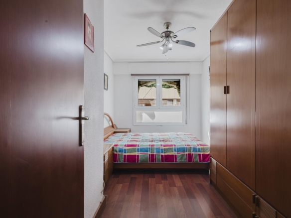 View into a small bedroom with a bed at the back, a multicolor plaid quilt, tall wooden wardrobes along both sides, and a ceiling fan overhead.