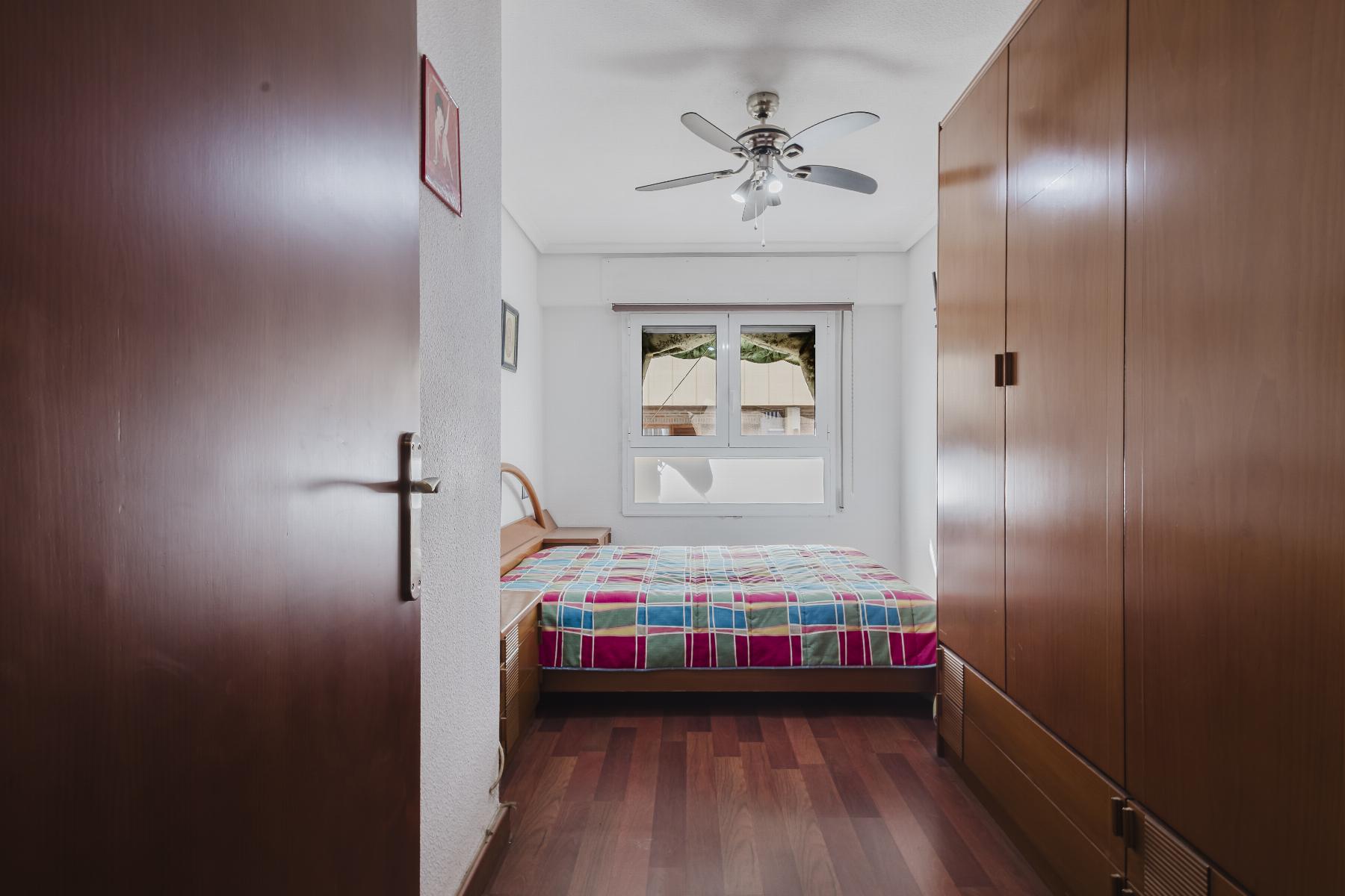 View into a small bedroom with a bed at the back, a multicolor plaid quilt, tall wooden wardrobes along both sides, and a ceiling fan overhead.